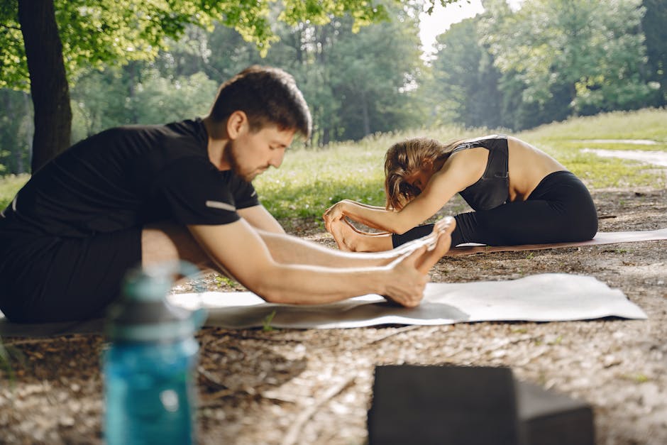 A man and woman practicing yoga outdoors in a sunny park, focusing on stretching