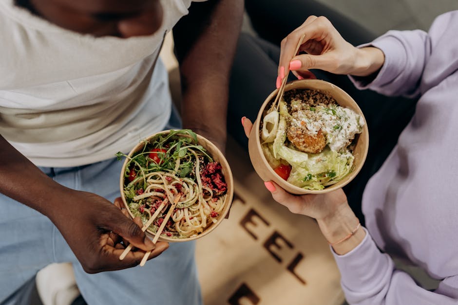 Two people holding bowls filled with salad and pasta, emphasizing healthy lifestyle choices