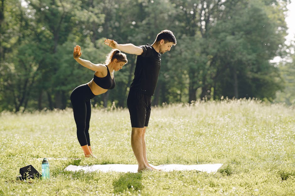 Man and woman doing yoga on grass in park, exercising together outdoors